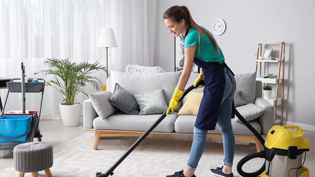 Female janitor with vacuum cleaner in room